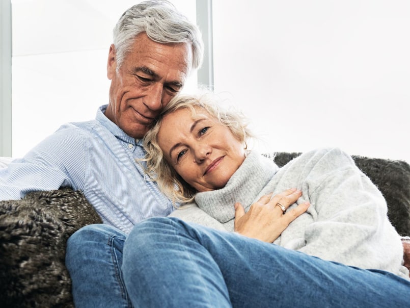 Mann und Frau liegen Arm in Arm kuschelnd auf dem Sofa und lächeln