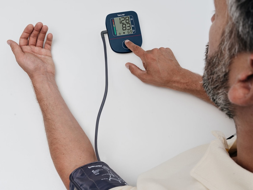 Mann misst seinen Blutdruck mit dem Beurer BM 25 Blutdruckmessgerät und drückt mit dem Finger auf das Gerät