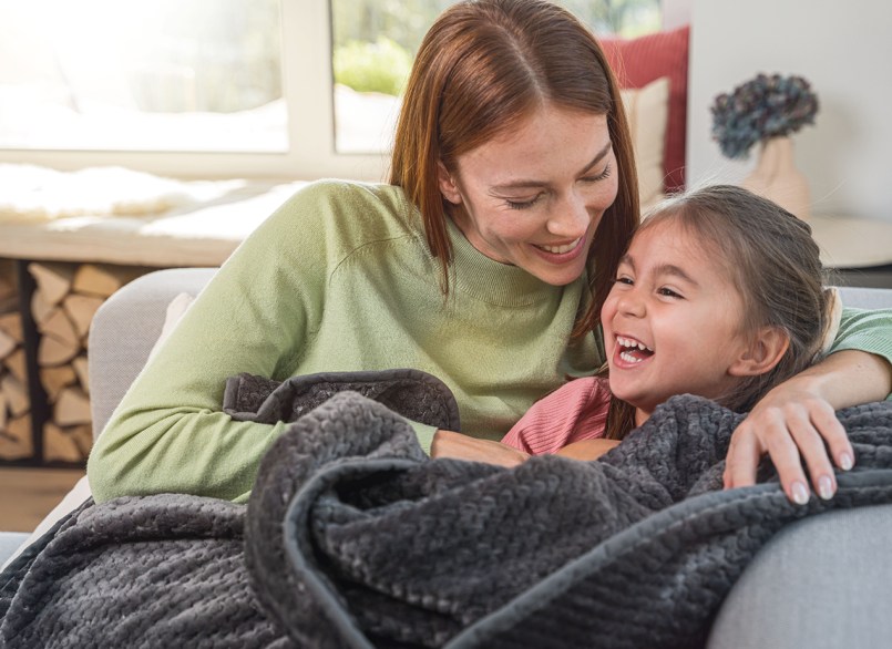 Frau und Kind kuscheln auf dem Sofa unter der dunkelgrauen Beurer Heizdecke HD 65
