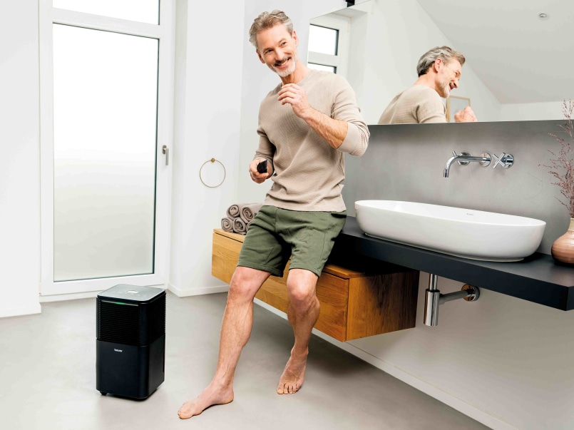 Ein Mann steht in einem modernen Badezimmer neben dem LE 150 Luftentfeuchter