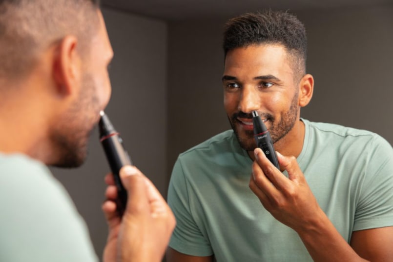 Mann trimmt die Nasenhaare mit dem Beurer MN3X und schaut dabei in den Spiegel im Badezimmer und lacht