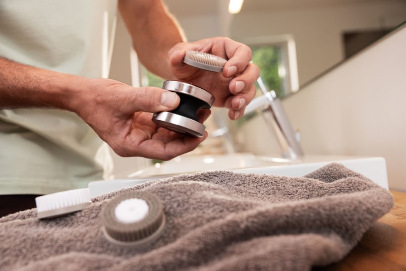 Hand wechselt Aufsätze der FC 59 im Badezimmer neben dem Waschbecken, er hält das Gerät und 1 Aufsatz in der Hand, 2 Aufsätze liegen daneben