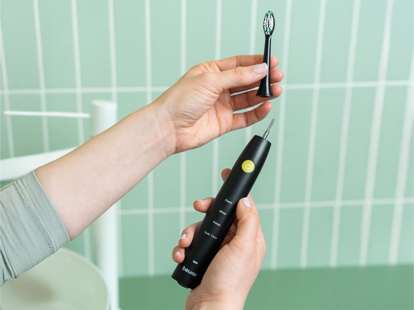 In einem mintgrün gefliesten Badezimmer steckt eine Person den Classic Clean Bürstenkopf auf die SC 30 Zahnbürste