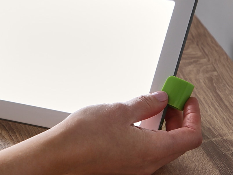 Hand befestigt eine grüne Halterung an der Ecke der rechteckigen Tageslichtlampe auf einem Holztisch.