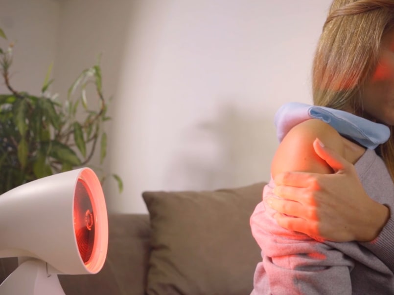 Frau hält sich ihren Oberarm, während eine IL 35 Infrarotlampe darauf gerichtet ist.