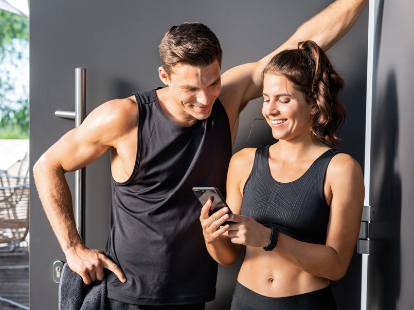 Ein Mann und eine Frau in Sportklamotten schauen lachend auf das Handy der Frau.
