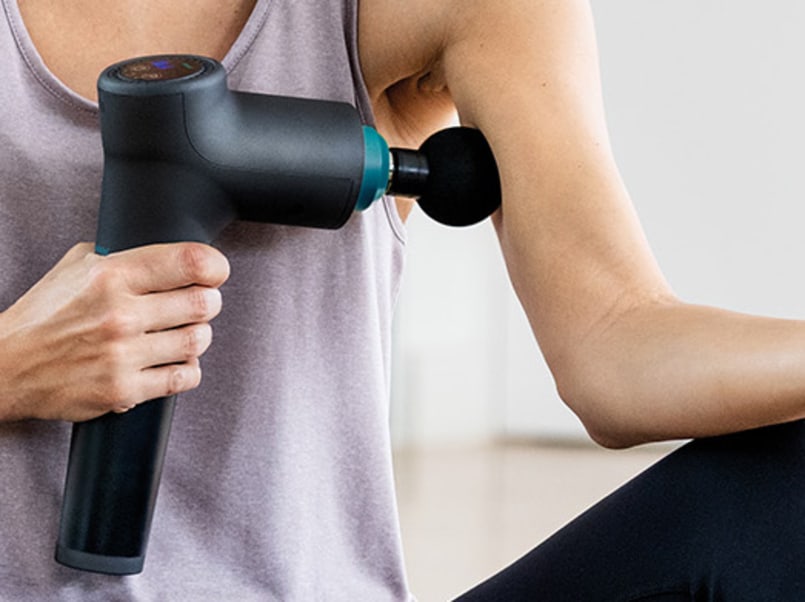 Frau wendet die Massage Gun am Oberarm an