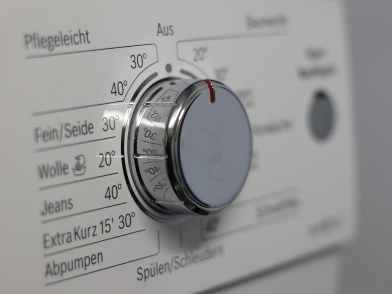 Nahaufnahme eines runden, silbernen Drehknopfs an einer Waschmaschine mit Temperatur- und Programmangaben.