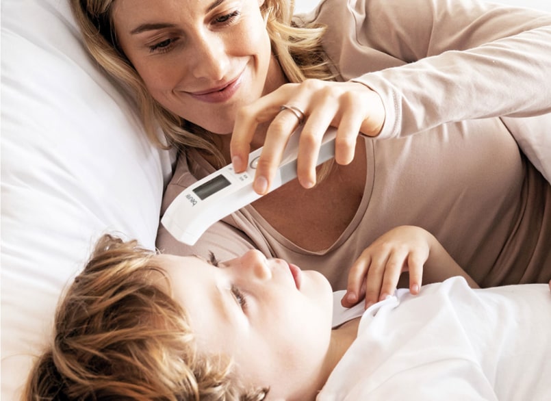 Frau misst Kind im Bett die Körpertemperatur