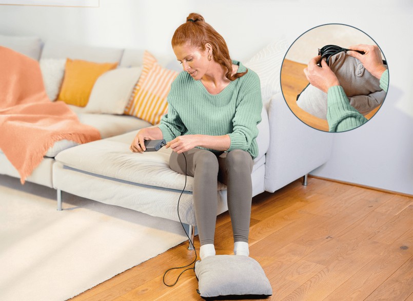 Eine Frau sitzt auf der Sofakante und verwendet das Fußmassagegerät, indem sie es an eine Powerbank anschließt