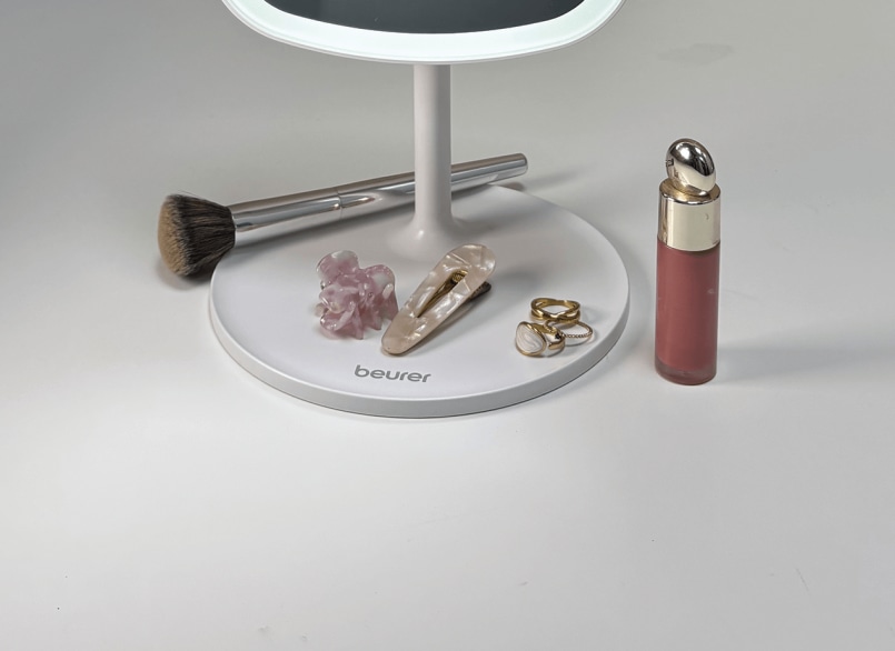 Ablagefläche des Kosmetikspiegels im Fokus mit einem Make-Up-Pinsel, einer Rouge-Tube, Haarklammern und goldenen Ringen