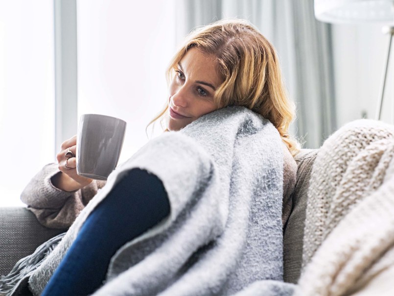Frau sitzt mit Tasse in der Hand auf dem Sofa