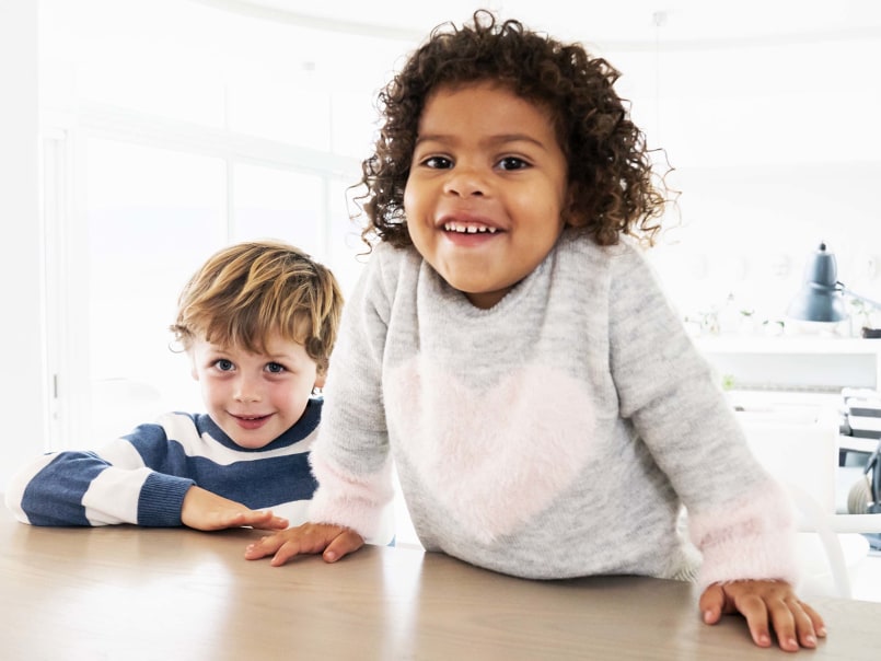 Zwei Kinder stützen sich auf dem Tisch ab und lächeln