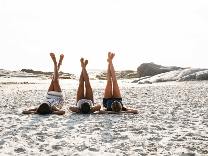 Drei Frauen liegen am Strand im Sand und strecken ihre Beine in die Luft