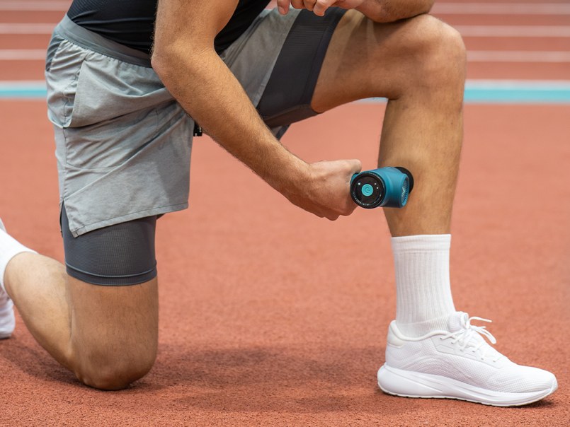 Mann sitzt auf Sofa und massiert seine Wade mit einer Massage Gun