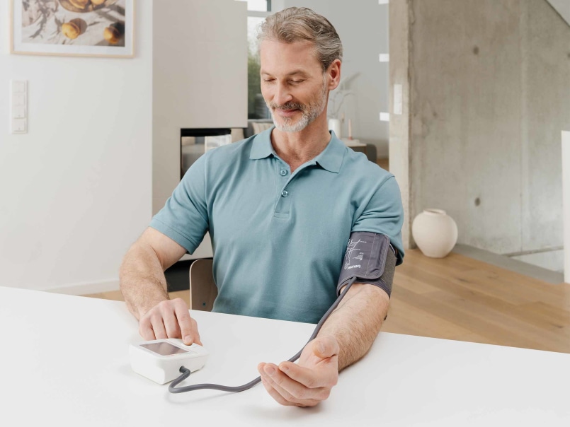 Mann sitzt am Tisch und misst seinen Blutdruck