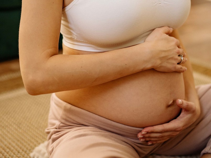 Schwangere Frau sitzt mit Händen schützend auf dem freiliegenden Bauch