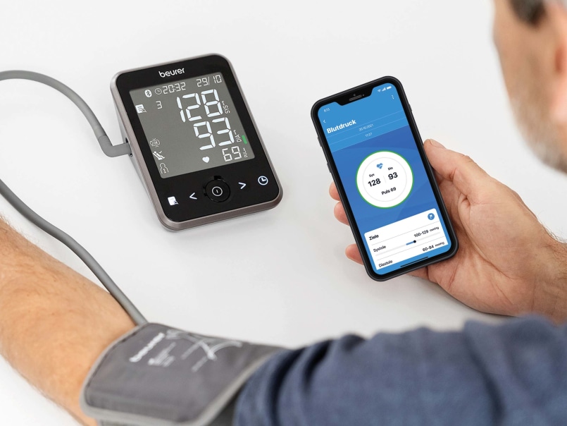 Blick über die Schulter, Mann mit Smartphone in der Hand misst Blutdruck mit dem Beurer BM 64, Smartphone zeigt Blutdruckwerte an