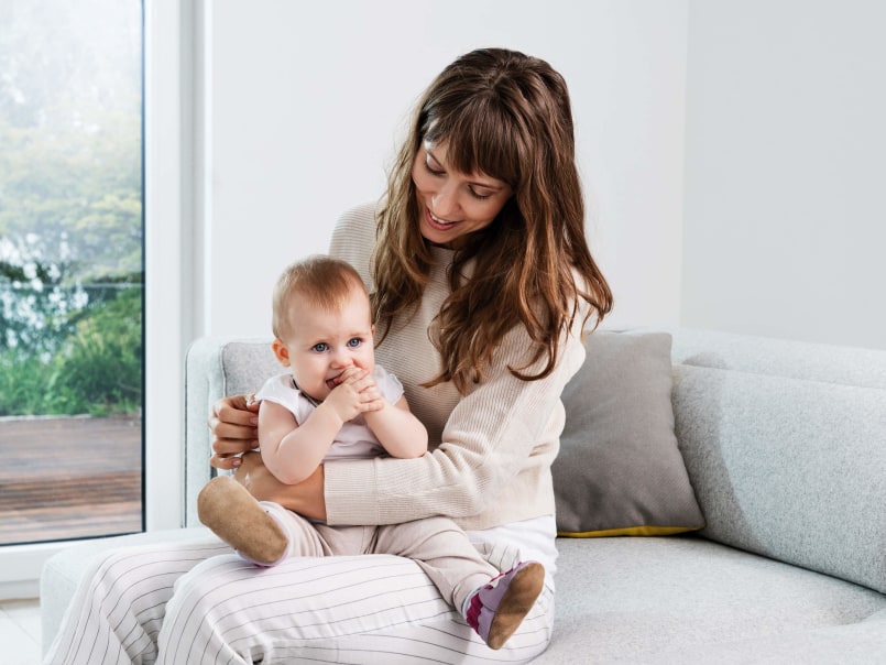Frau sitzt auf einem Sofa und hält ein Baby auf dem Schoß