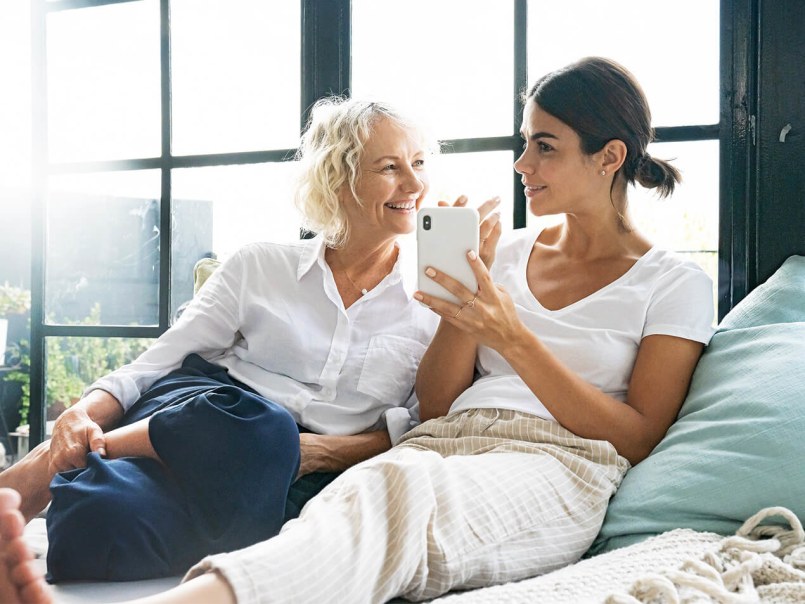 Mutter und Tochter mit Smartphone in der Hand auf dem Sofa