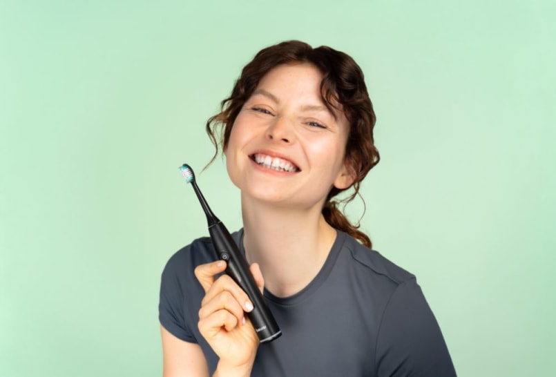 Junge Frau hält strahlend die Schallzahnbürste SC 50 von Beurer neben ihr Gesicht