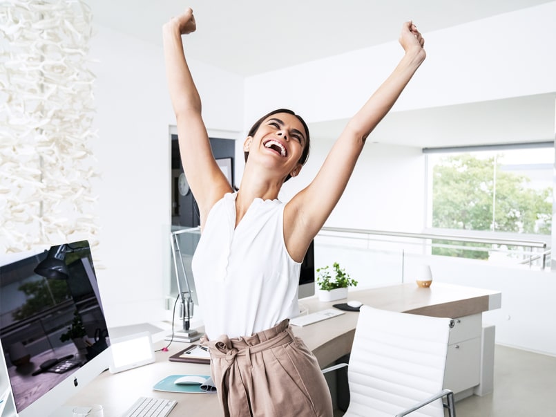 Junge Frau die, die arme in die höhe streckt und einen freudigen Gesichtsausdruck hat.