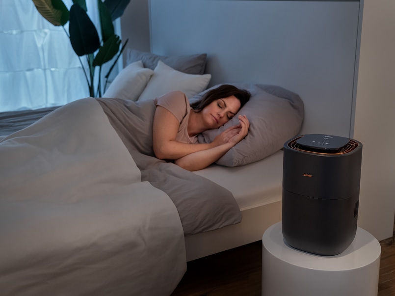 Eine Frau liegt im Bett und hat die Augen geschlossen. Der LB 300 steht auf einem Beistelltisch davor.