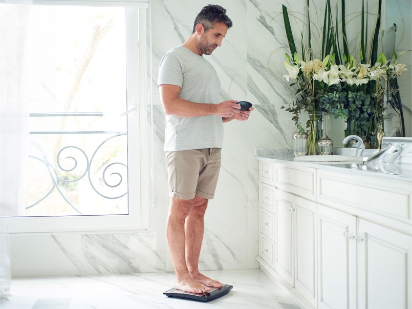 Mann steht auf Waage mit dem abnehmbaen Handteil in den Händen