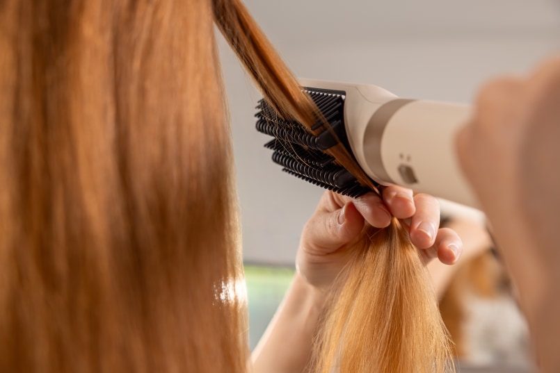 Gros plan d’une femme aux cheveux orange se brossant les cheveux avec une brosse lissante