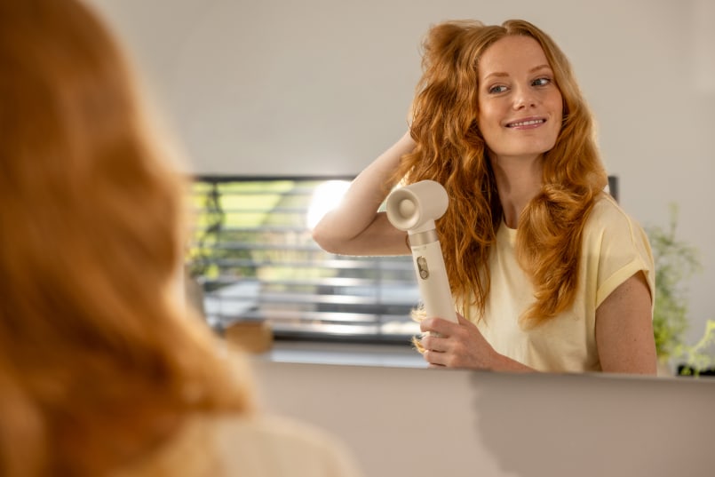 Une femme se tient devant le miroir et se coiffe les cheveux