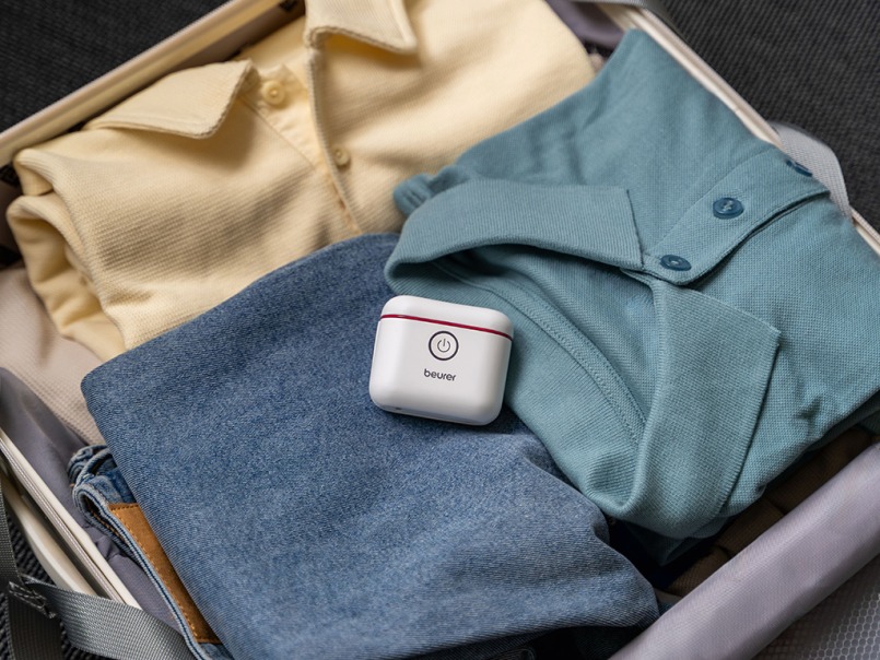 Der kompakte weiße Beurer MP 10 elektrische Nagelnknipser liegt mittig in einem gepackten Koffer mit einem gelben und einem türkisen Poloshirt und einer Jeans