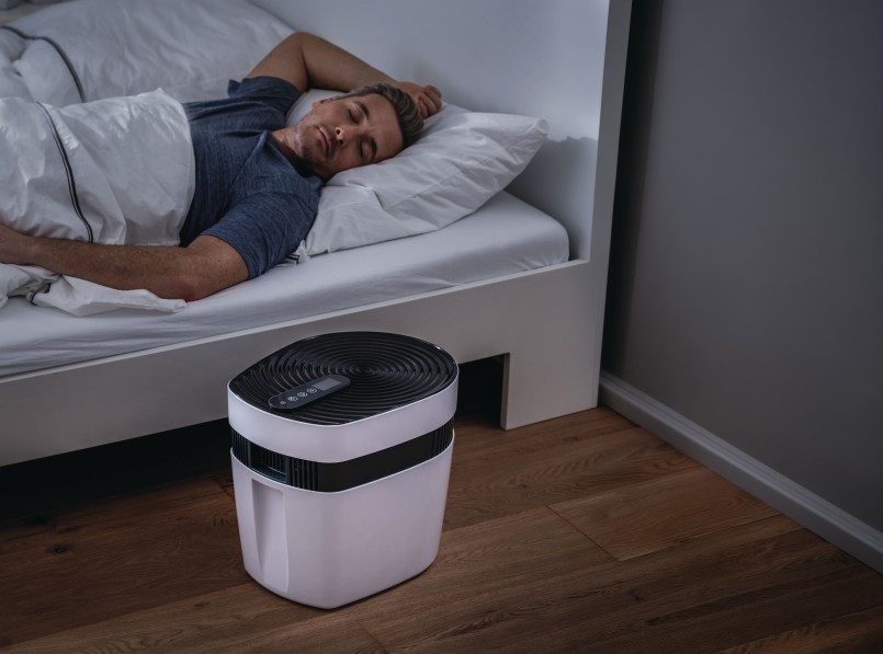 Ein erwachsener Mann liegt in entspannter Position einem Bett und hat die Augen geschlossen. Neben dem Bett steht das maremed® Meeresklimagerät.