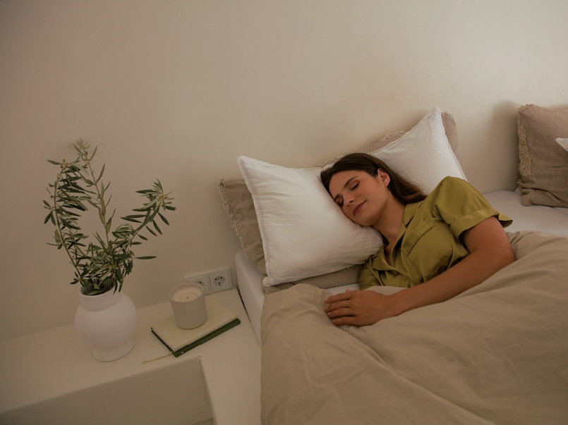 Una giovane donna è sdraiata di lato a letto. Ha gli occhi chiusi.
