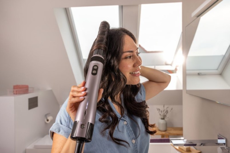 Frua con i capelli scuri è davanti allo specchio e si acconcia i ricci con l’accessorio arricciacapelli del multistyler.