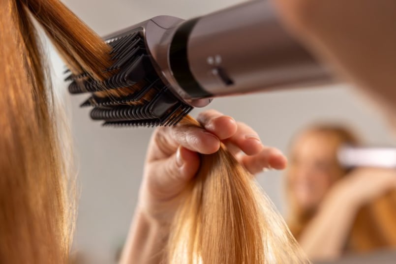 Primo piano di una donna con capelli arancioni che passa la Spazzola lisciante tra i capelli
