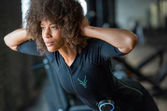 A woman performs a back workout with the Antelope EMS suit in a fitness centre.