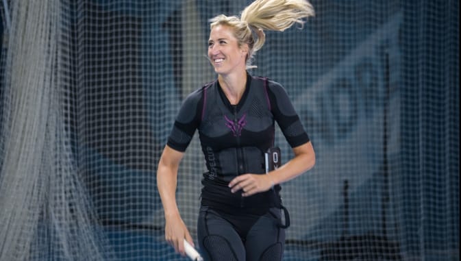 Sophia Bergner durante l'allenamento di tennis con la tuta EMS wireless di Antelope. È visibile dal davanti fin sopra le ginocchia e guarda di lato con un sorriso. Tiene una racchetta da tennis nella mano destra.