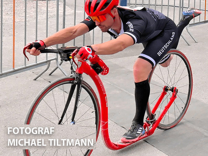 Andreas Böhm profiteert van EMS-training met Antelope tijdens een scooterrace. Hij is iets opzij te zien in het midden van de foto, van top tot teen op een step. Op de achtergrond is een grijs hek te zien.