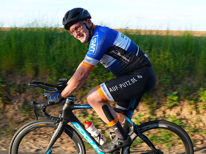 Stefan Feilen achieves a good performance in the ultra-distance cycling race after preparing with EMS training from Antelope. He can be seen in the centre of the picture from the side on his racing bike, smiling at the camera. A meadow can be seen in the background.