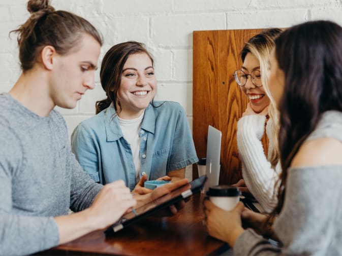 The picture shows four people sitting together at a table in an office. They are discussing a project, a young man is holding a tablet in his hands.