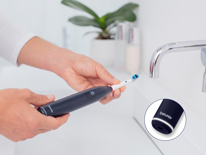 Elektrische Zahnbürste die über einem Waschbecken gehalten wird und eine Nahaufnahme der LED-Ladeanzeige