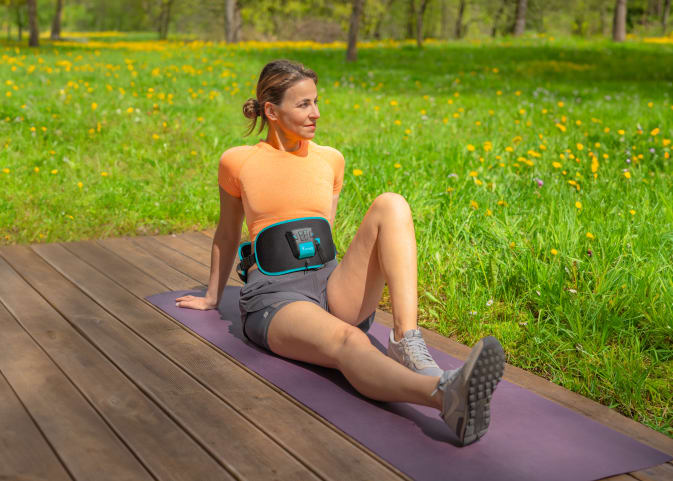 A woman takes a break from her core workout with the Corefit II EMS belt from Antelope.