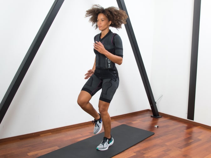 A woman performs knee lifts in the Antelope EMS suit in her home.