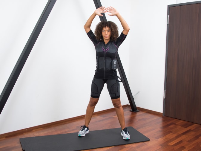 A woman performs Jumping Jacks in the Antelope EMS suit in her home.