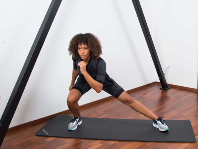 A woman performs side lunges in the Antelope EMS suit in her home.