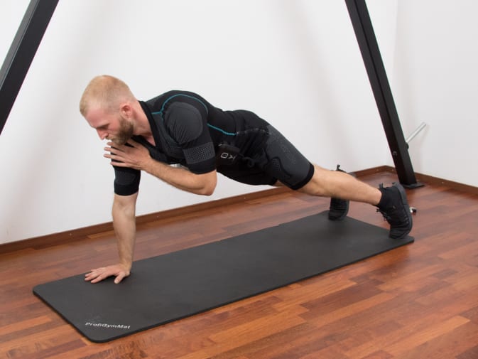 A man performs Plank Shoulder Taps in the Antelope EMS suit in his home.
