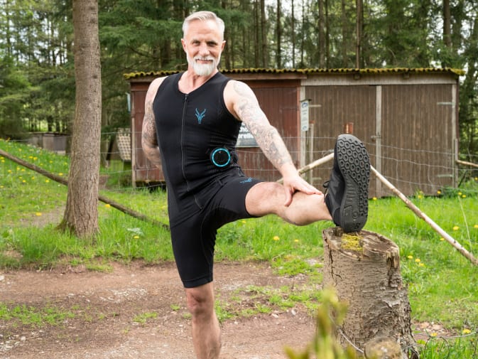 A man trains outdoors with the EMS suit from Antelope and stretches in the process.