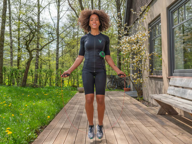 Eine Frau führt mit einem Springseil ein EMS Fitness Workout im Garten durch.