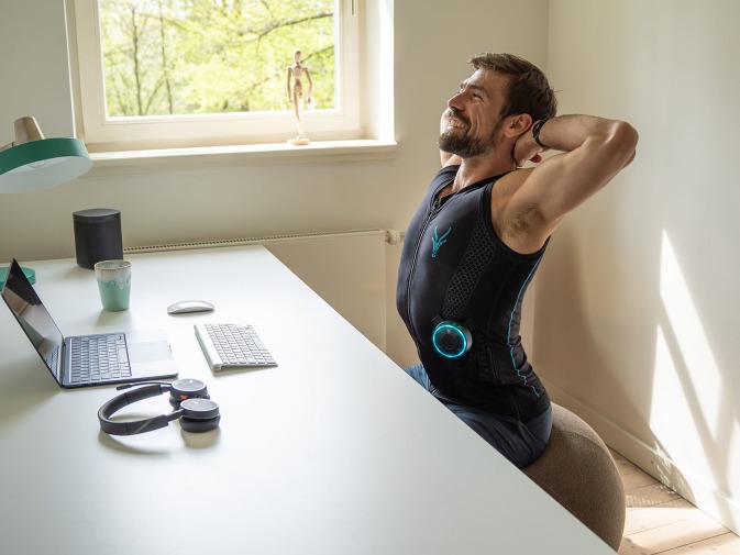 A man performs simple stretching exercises with the EMS suit from Antelope to relieve tension in her back.