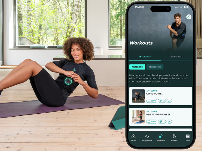 a woman in an EMS suit trains at home, next to her a mobile phone screen with the workouts in the Antelope Go app
